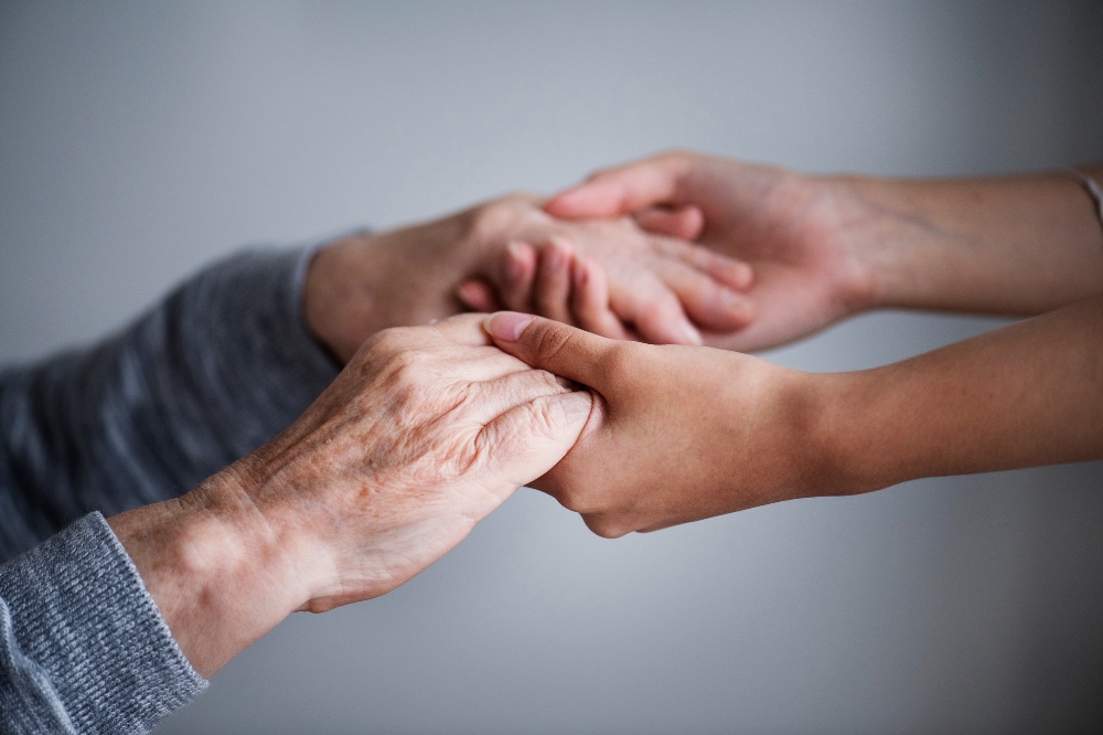 Close-up of two people's hands clasped together in a supportive, caring gesture.